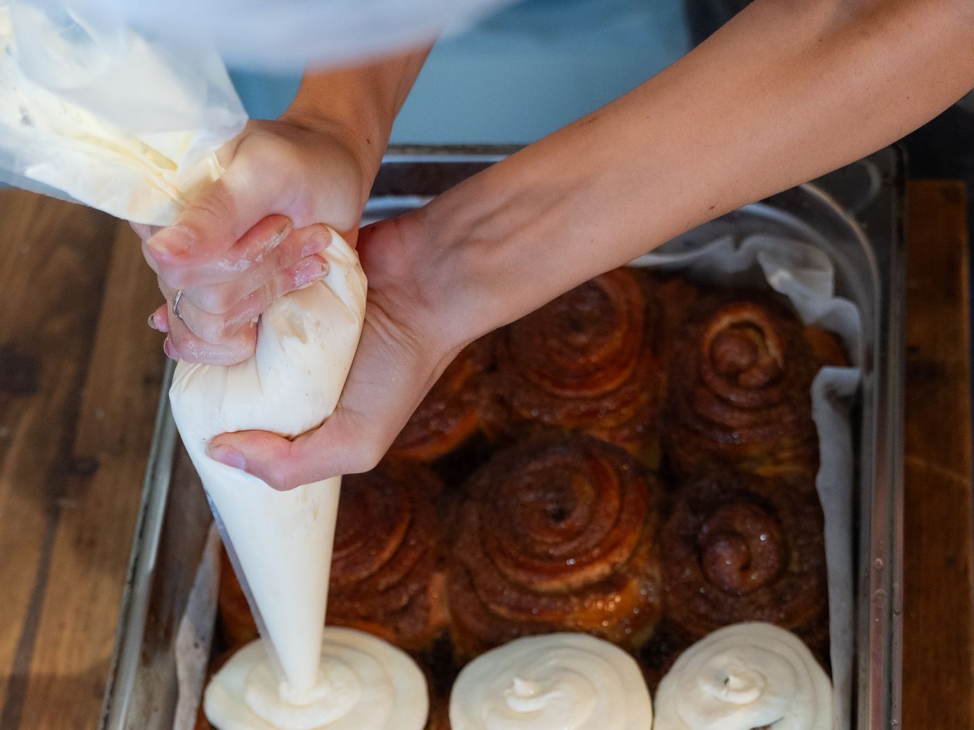 A chef piping cream over freshly baked cinnamon rolls