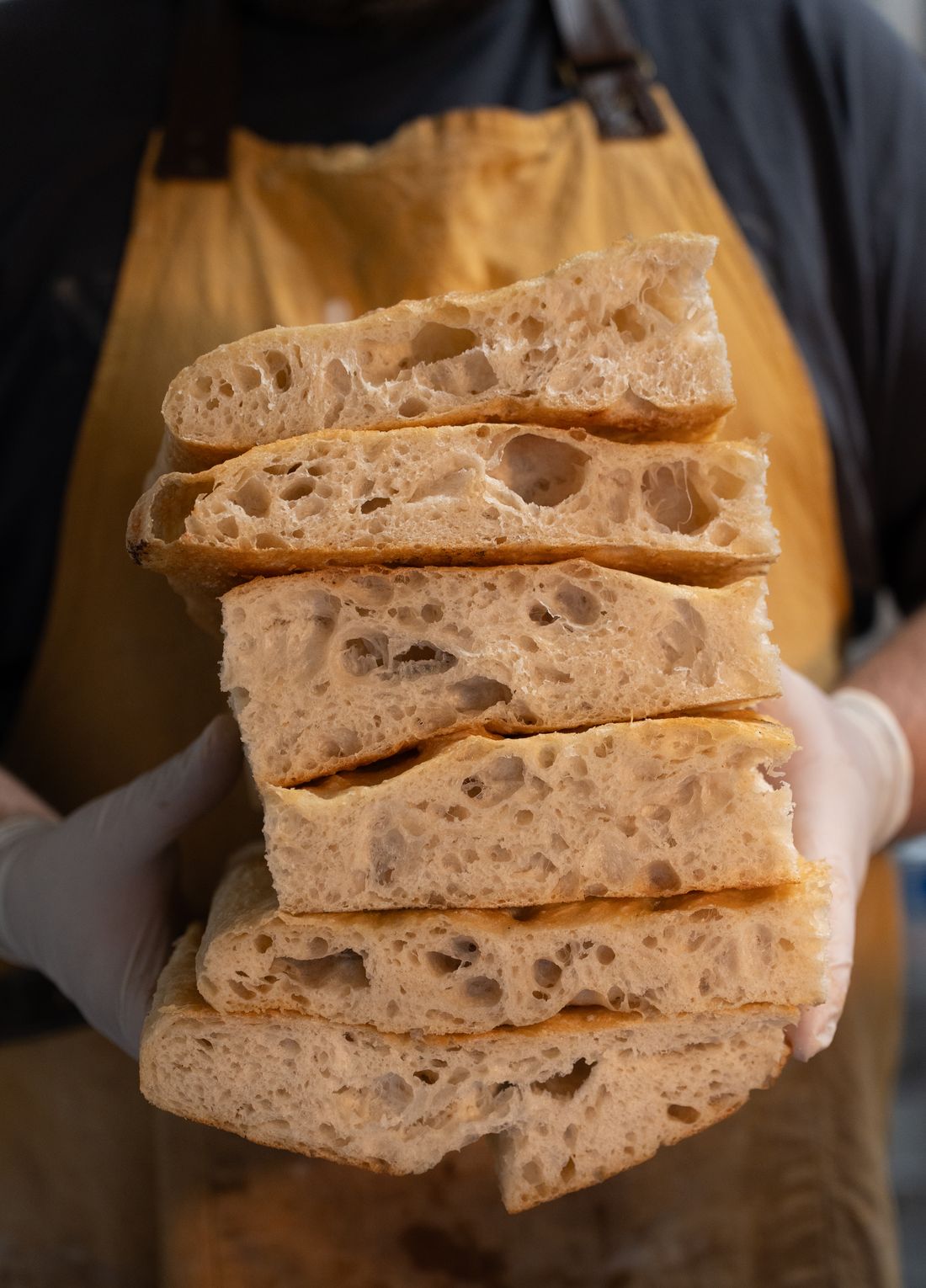 A baker holding a stack of freshly cut focaccia