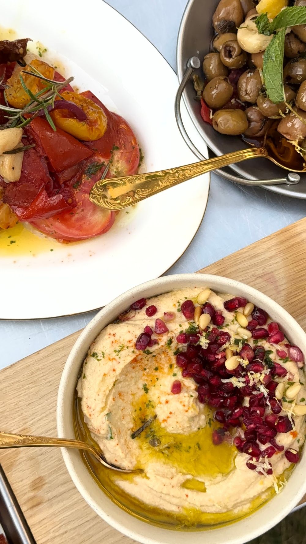 Overhead view of roasted tomatoes, marinated olives and a bowl of hummus with pomegranate