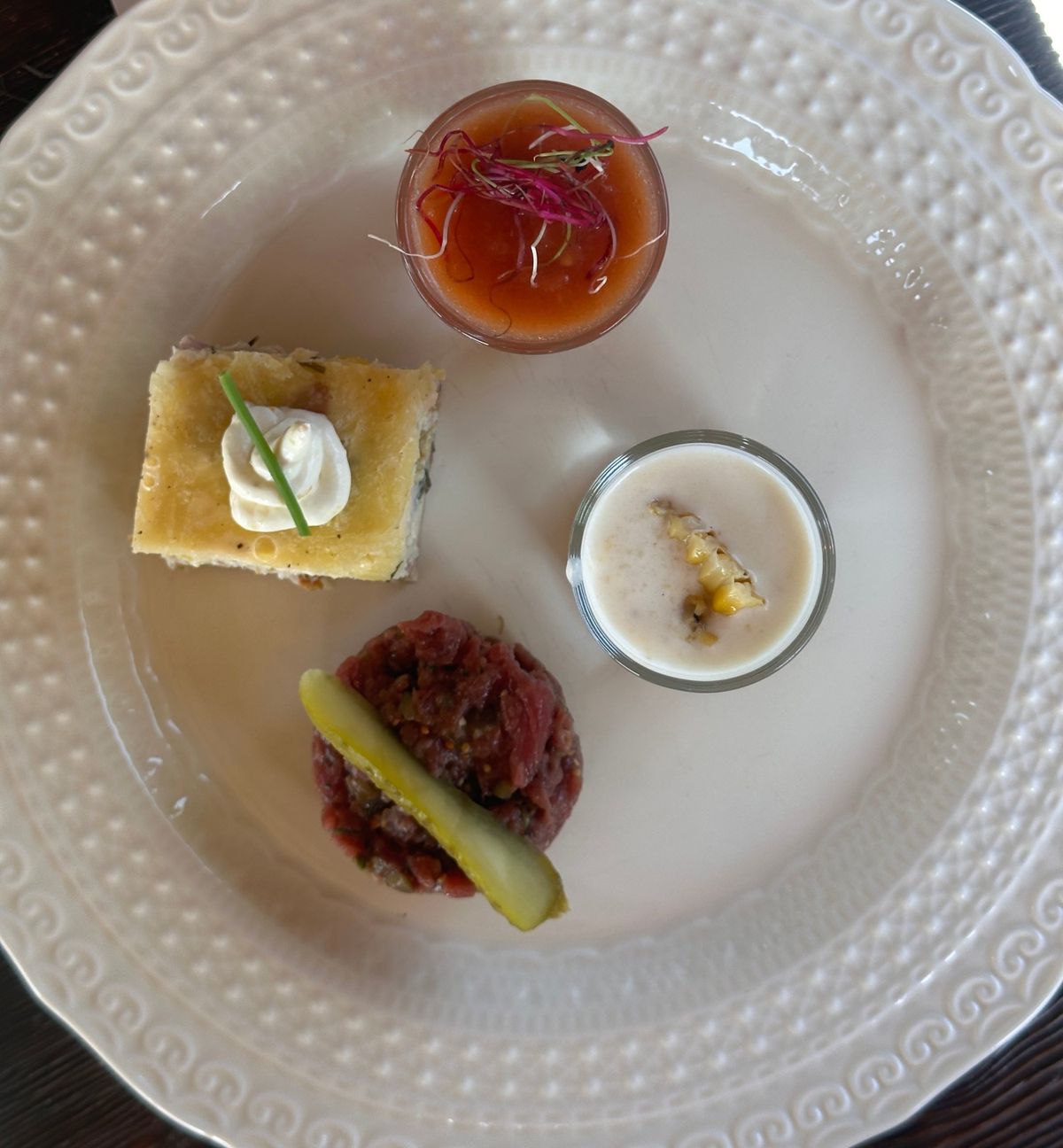 Overhead view of a tasting plate with two soups in glasses, a savoury tart and a beef tartare